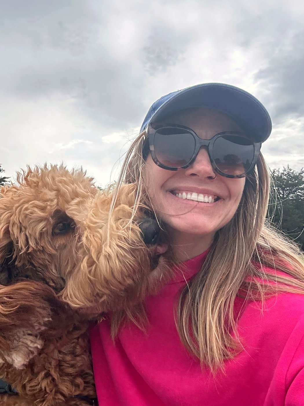 Crystal, the Choptank Paws owner, grinning in a ball cap with a curly red doodle pressed against her cheek.